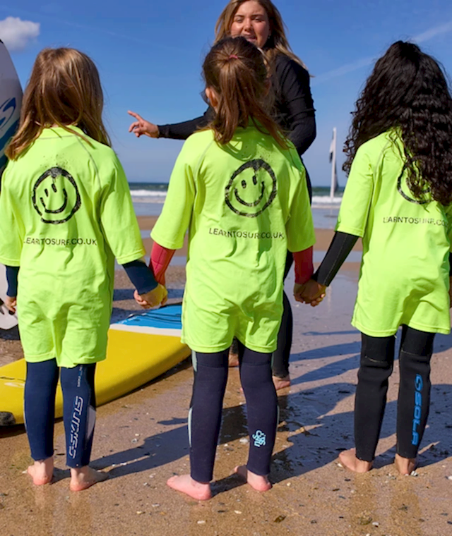 Three kids on a beach getting a surfing lesson