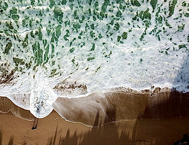 Birds-eye drone image of waves breaking on a beach.