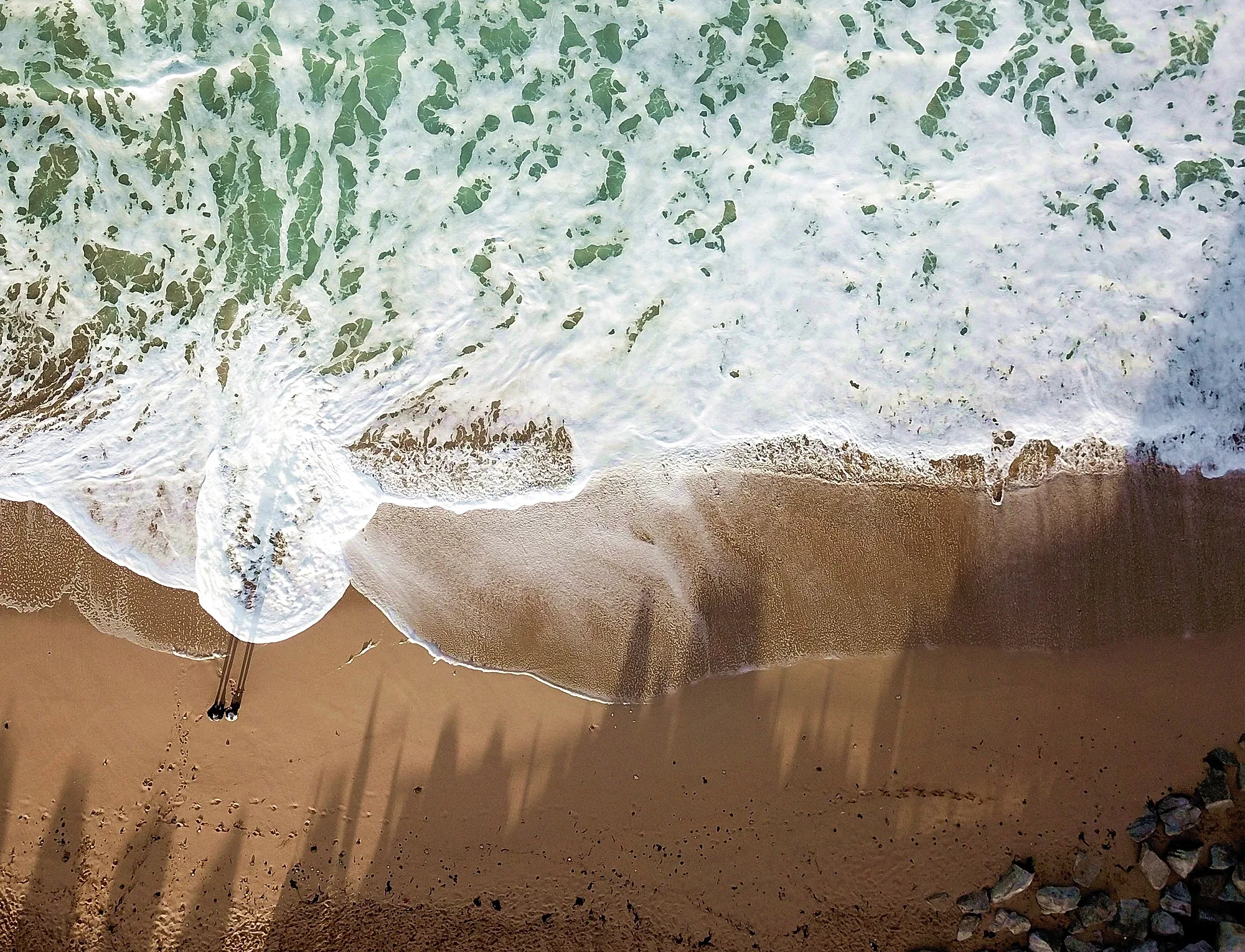 Birds-eye drone image of waves breaking on a beach.