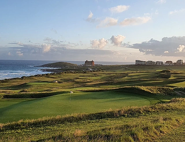 Drone image of a big stretch of a sunny, green golf course with views of the sea and the Cornish coast. On the horizon, you can see the Headland Hotel. 