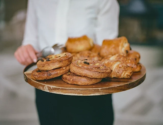Handcrafted French pastries on a rustic wooden serving tray at a bakery, featuring pain au chocolat and almond croissants.