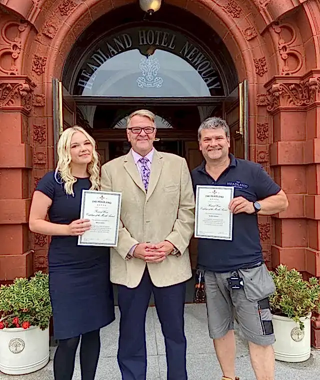 Three people standing outside the Headland Hotel Entrance celebrating an award