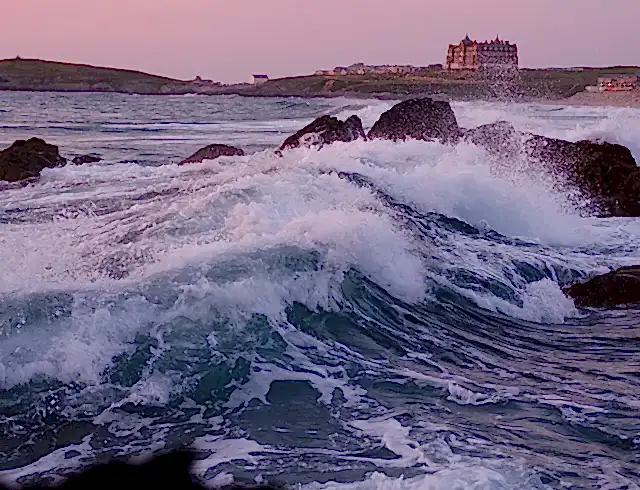 Stormy ocean with waves crashing against the rocks. Pink morning sunrise. 