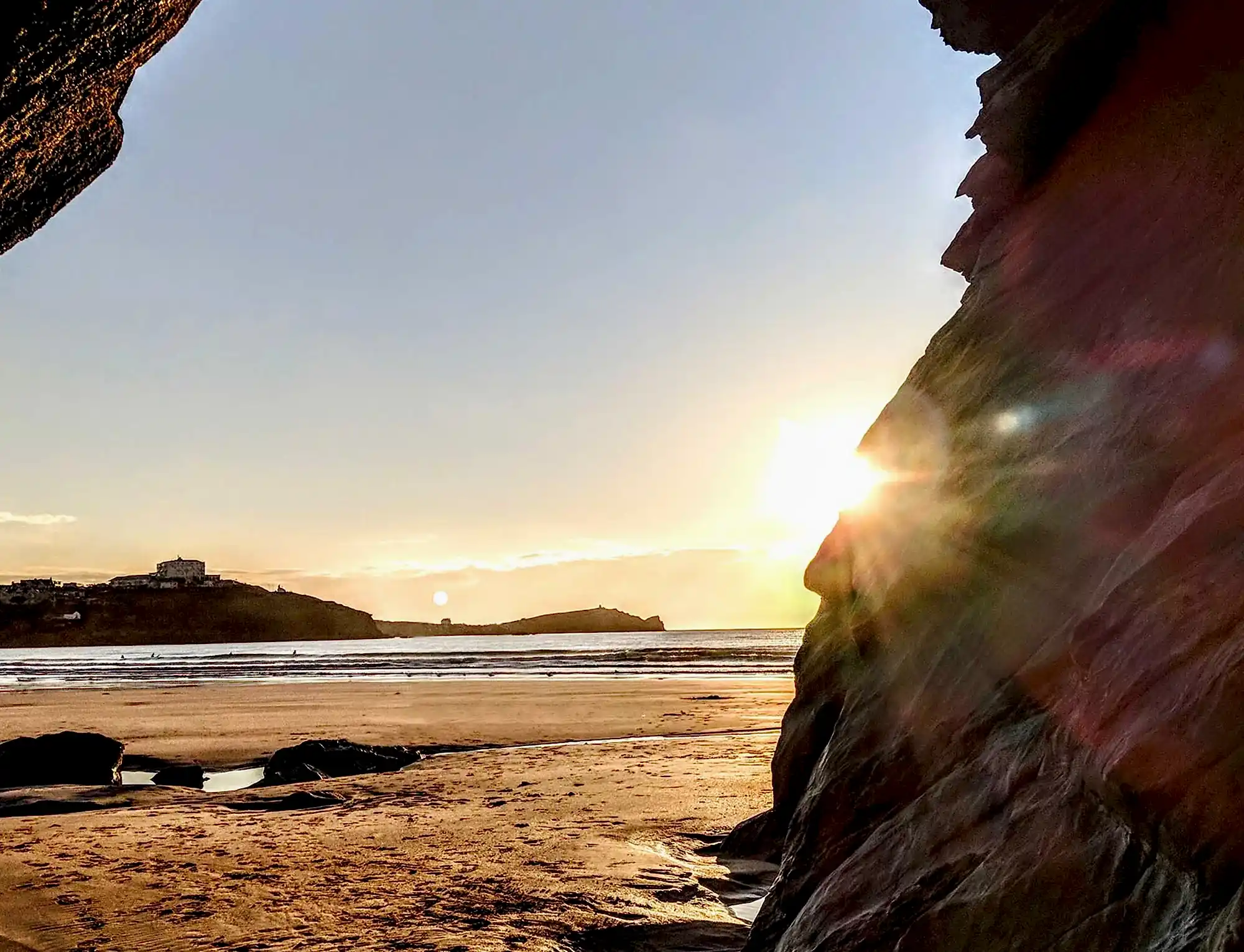 A view of the beach from behind a rock with the sun shining