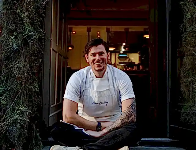 a chef sitting proudly outside the entrance to the dining area