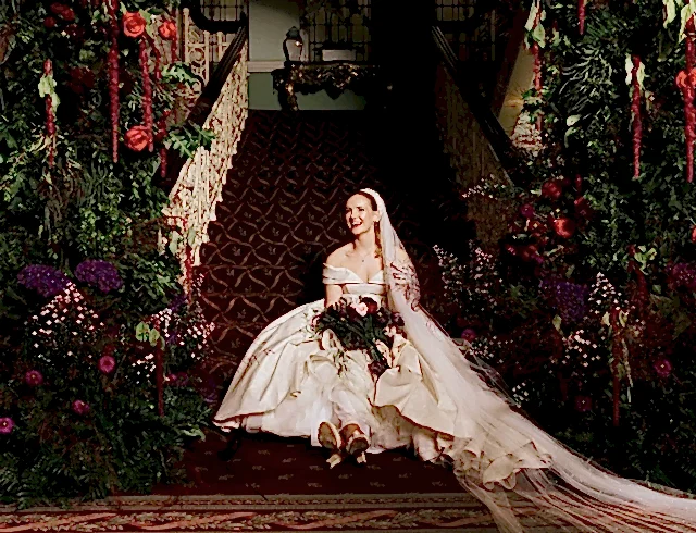 A bride sitting at the bottom of a set of velvet coated stairs holding a bouquet