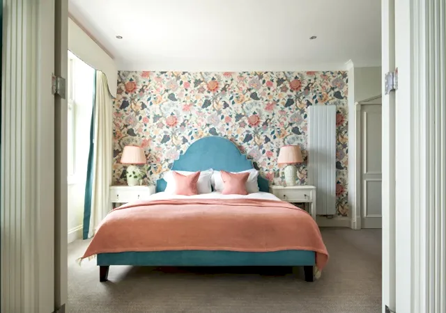 Luxury Ocean Suite hotel bedroom featuring vibrant floral wallpaper, a teal arched headboard and pink accents in a modern coastal design.