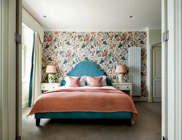 Luxury Ocean Suite hotel bedroom featuring vibrant floral wallpaper, a teal arched headboard and pink accents in a modern coastal design.