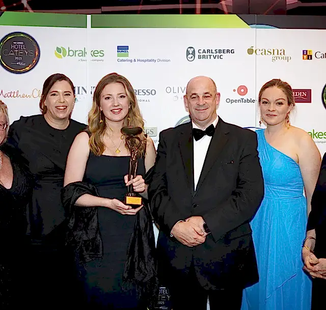 Winners of the Sustainable Hotel of the Year posing with their trophy in front of They Cateys logo wall at an evening awards event.