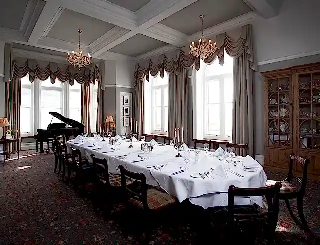 A full length dining table in a huge room with a grand piano