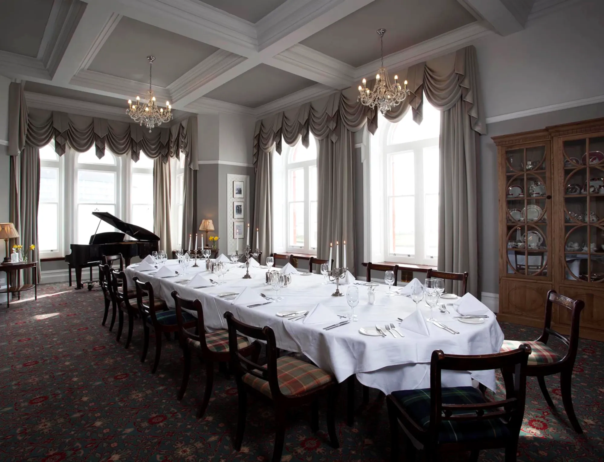 A full length dining table in a huge room with a grand piano