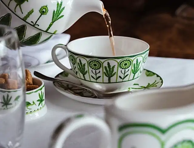 a teapot pouring tea into a cup and saucer on a white table