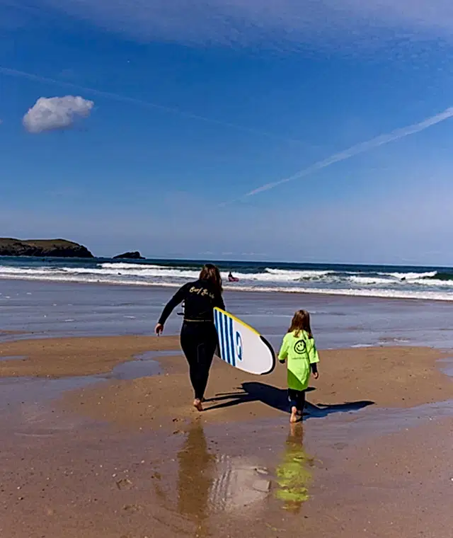 a lady and a girl on a sunny beach with a surfboard