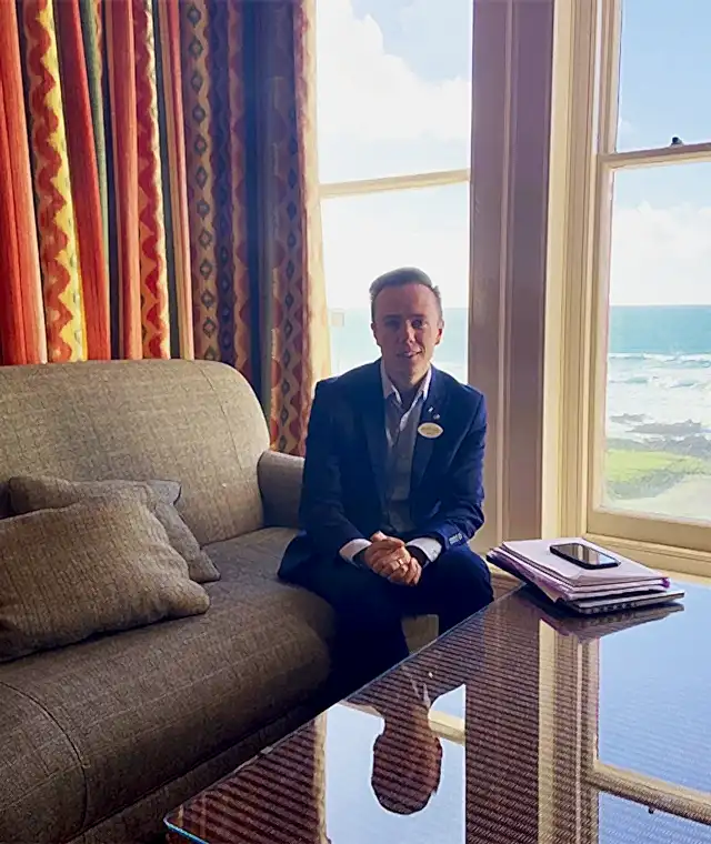 A man sitting on a sofa in a room overlooking the bay at the Headland Hotel