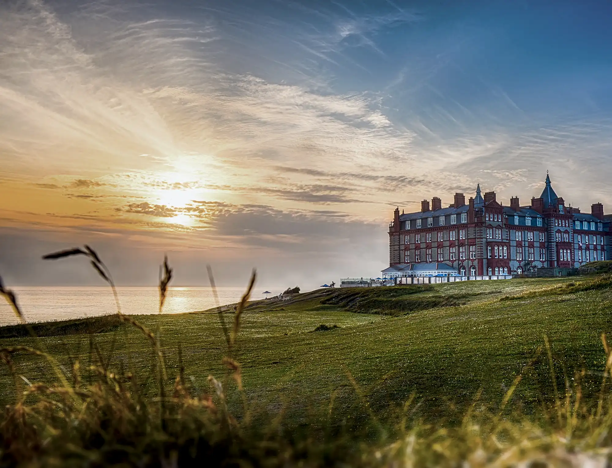 Sunset view of the Headland Hotel in Newquay, Cornwall, overlooking the Atlantic Ocean, coastal cliffs and golf course.